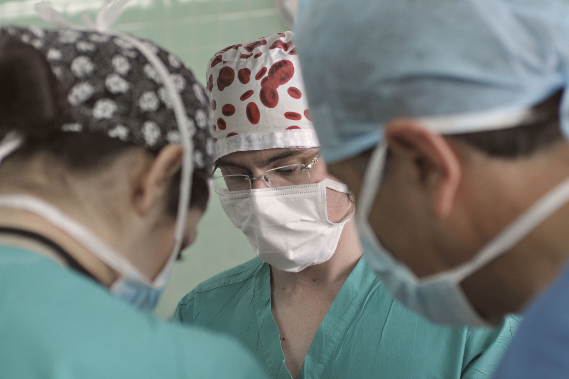 Team of doctors in surgical attire performing a medical procedure in an operating room.